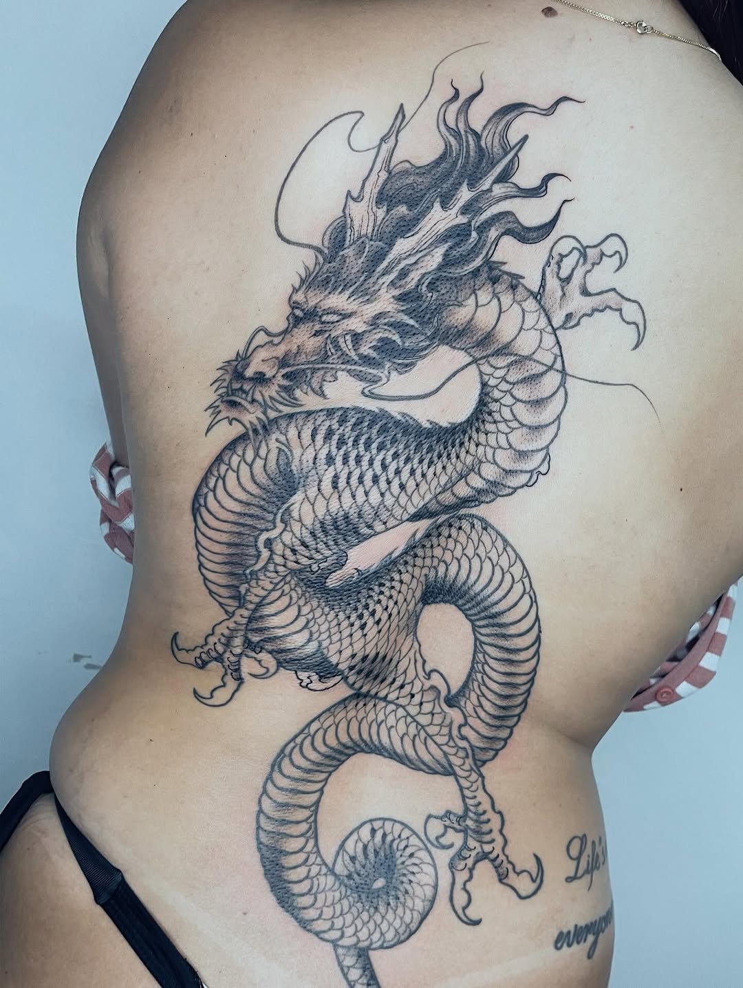 Tatuagem autoral de dragão oriental em blackwork e fineline ocupando as costas inteiras, executada na Flag Haus, Vila Mariana, São Paulo
