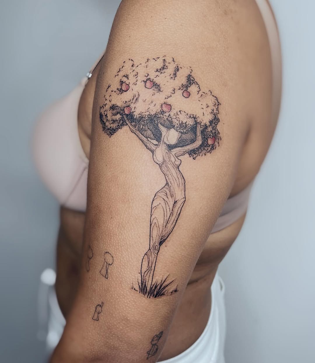 Tatuagem autoral de árvore da vida no braço, com figura humana formando o tronco e folhagem com maçãs como copa, executada pelo tatuador Julio Bandeiras na Flag Haus, Vila Mariana, São Paulo