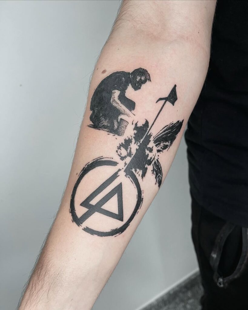 Tatuagem blackwork no antebraço com figura segurando machado, pássaro em movimento e logo do Linkin Park, feita por Julio Bandeiras na Flag Haus