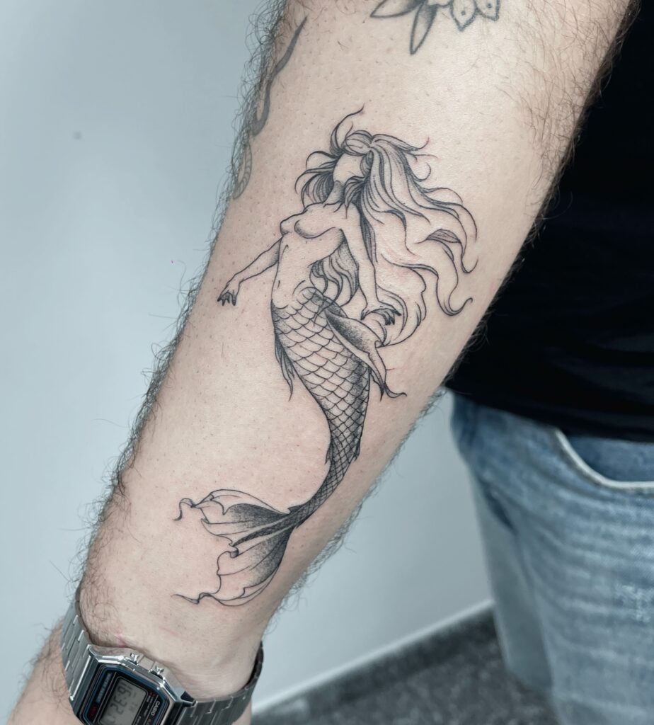 Tatuagem autoral de sereia no antebraço, em traço fino com escamas e sombreado em pontilhismo, trabalho de Julio Bandeiras na Flag Haus