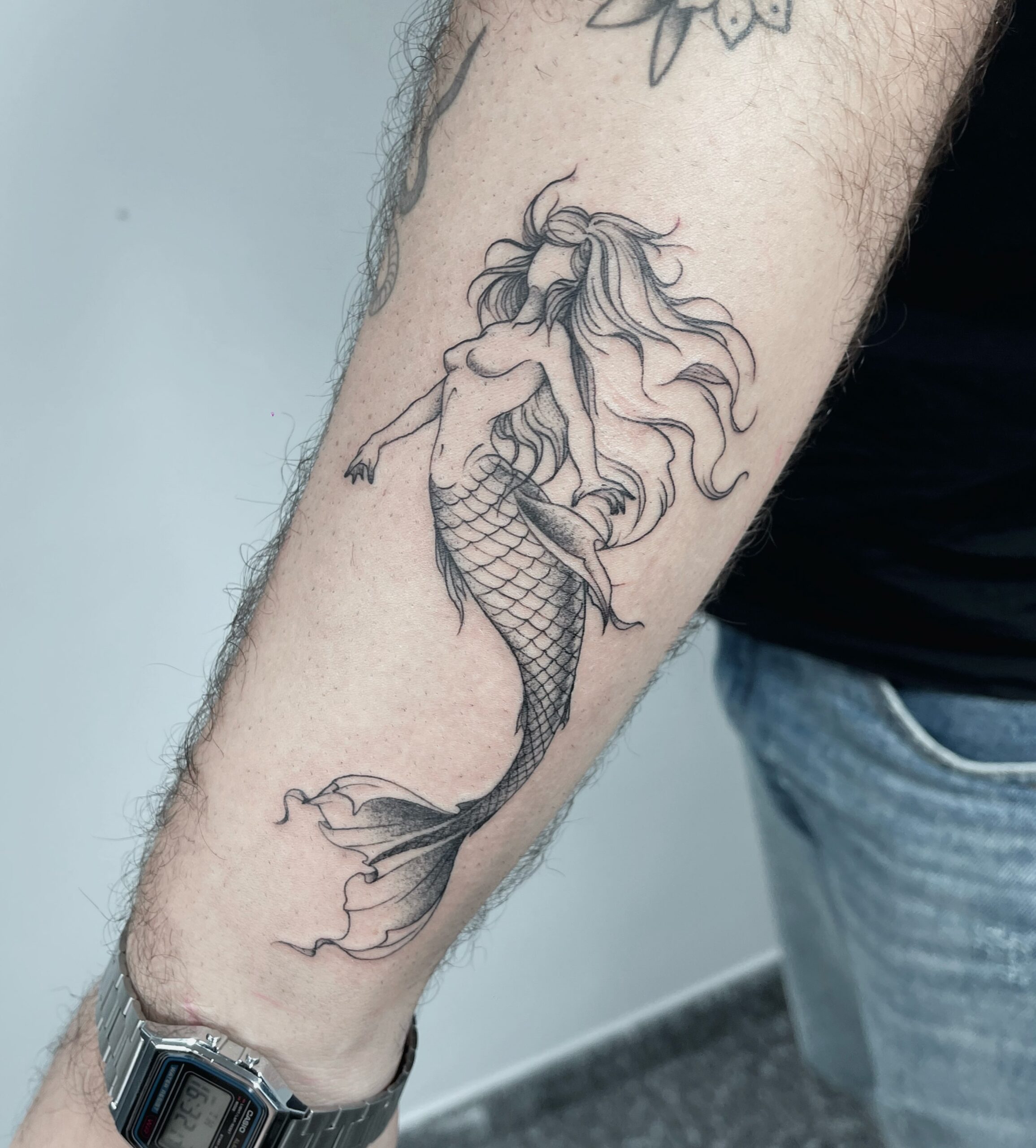 Tatuagem autoral de sereia no antebraço, em traço fino com escamas e sombreado em pontilhismo, trabalho de Julio Bandeiras na Flag Haus